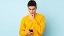 Junger Mann mit gelbem Pullover schaut auf sein Handy