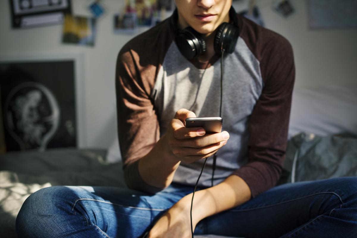 Junge mit Smartphone Junge sitzt mit Smartphone in der Hand auf dem Bett