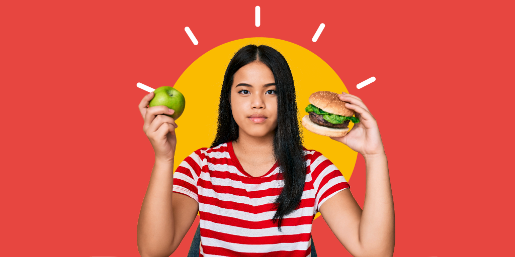 Ein junge Frau hält in einer Hand einen Burger und in der anderen ein Stück Obst.