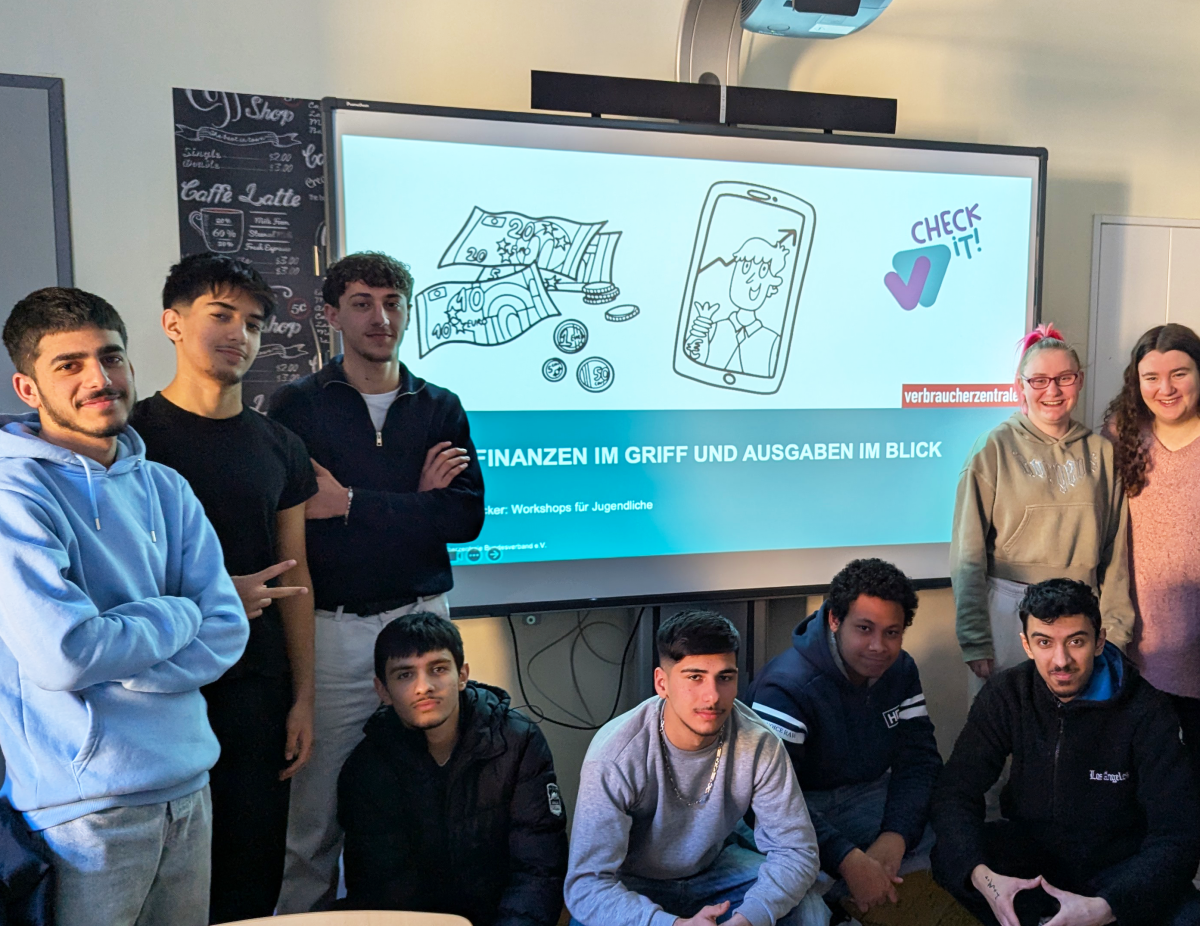 Schüler:innen stehen an einem Smartboard, auf dem die Workshop-Präsentation Finanzen im Griff und Ausgaben im Blick zu sehen ist.