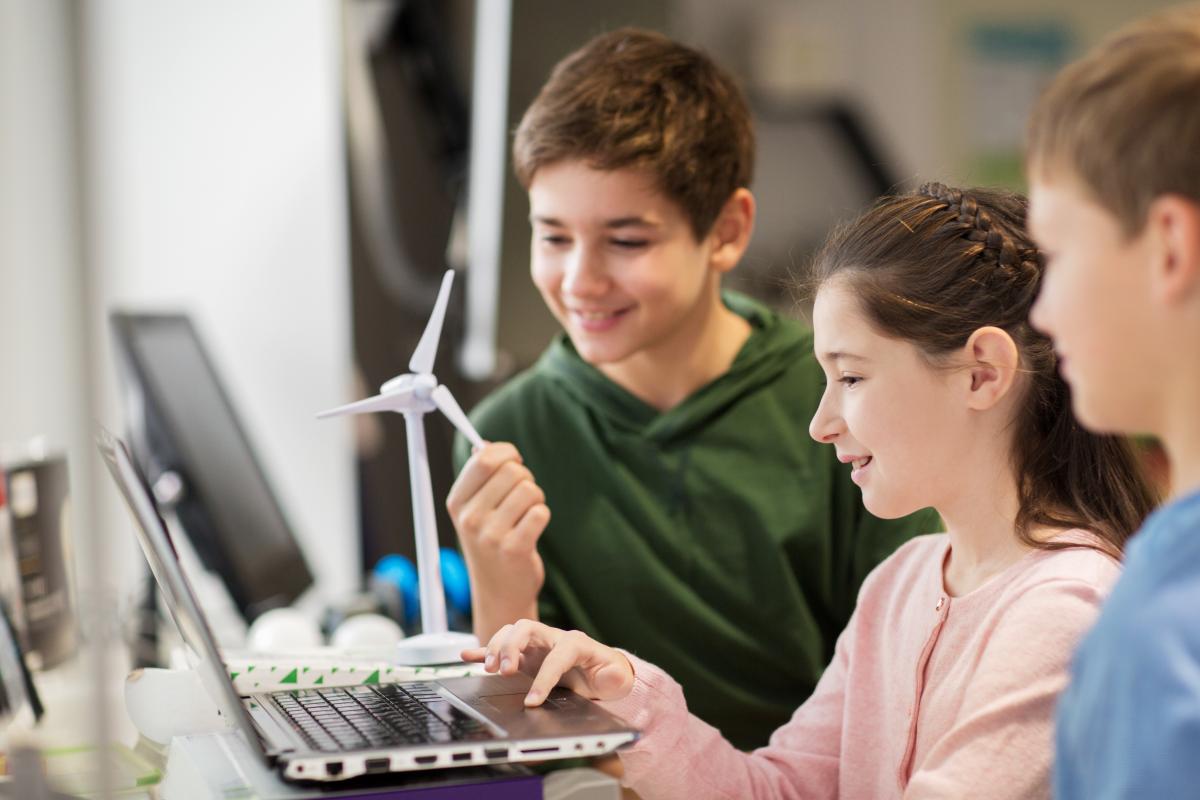 drei Schüler schauen in einen Laptop, ein Windkraftmodell steht auf dem Tisch