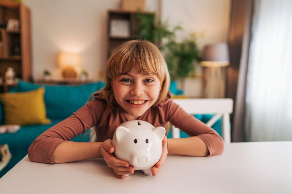 Ein Kind zeigt fröhlich und stolz ein Sparschwein.
