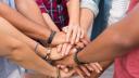 Eine Gruppe junger Menschen hat die Hände übereinander gelegt als Zeichen des Zusammenhalts.
