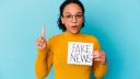 junge Frau hält Schild mit Begriff Fake News hoch