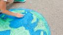 Ein Kind malt mit Kreide eine Weltkugel auf den Aspahlt.