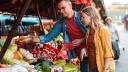 Junge Frau und junger Mann suchen gemeinsam an einem Marktstand Gemüse aus