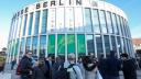 Zu sehen ist die Messe Berlin, am Gebäude hängt ein großes Plakat der Grünen Woche. Vor dem Gebäude sieht man mehrere Personen stehen.