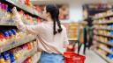 Junge Frau steht vorm Supermarktregal voller Nudelpackungen und greift nach einer Nudelpackung