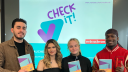 Vier junge Erwachsene stehen vor einem Smartboard, auf dem das Check-it-Visual der Verbraucherchecker und das Verbraucherzentrale-Logo zu sehen sind. Sie schauen lächelnd in die Kamera und halten den Action Planner, das Lernmaterial der Peer-Scout-Ausbildung, in den Händen.