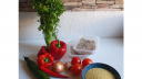 Auf einem Tisch liegen Paprika, Zwiebel, Gurke, Peperoni, Tomaten, Ingwer, Petersilie, Couscous und veganes Hähnchen. 